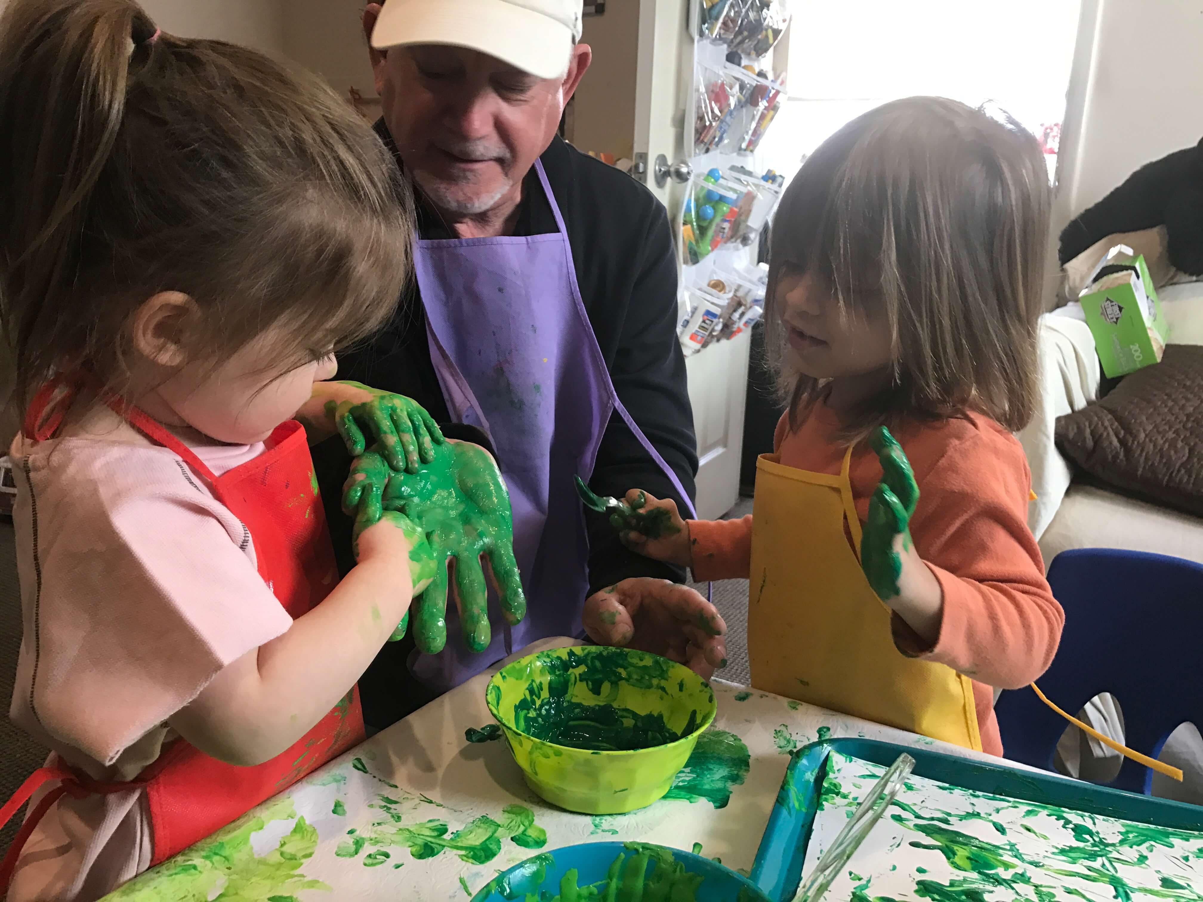 2 children paiting teacher's hand with green paint at early childhood development associates class