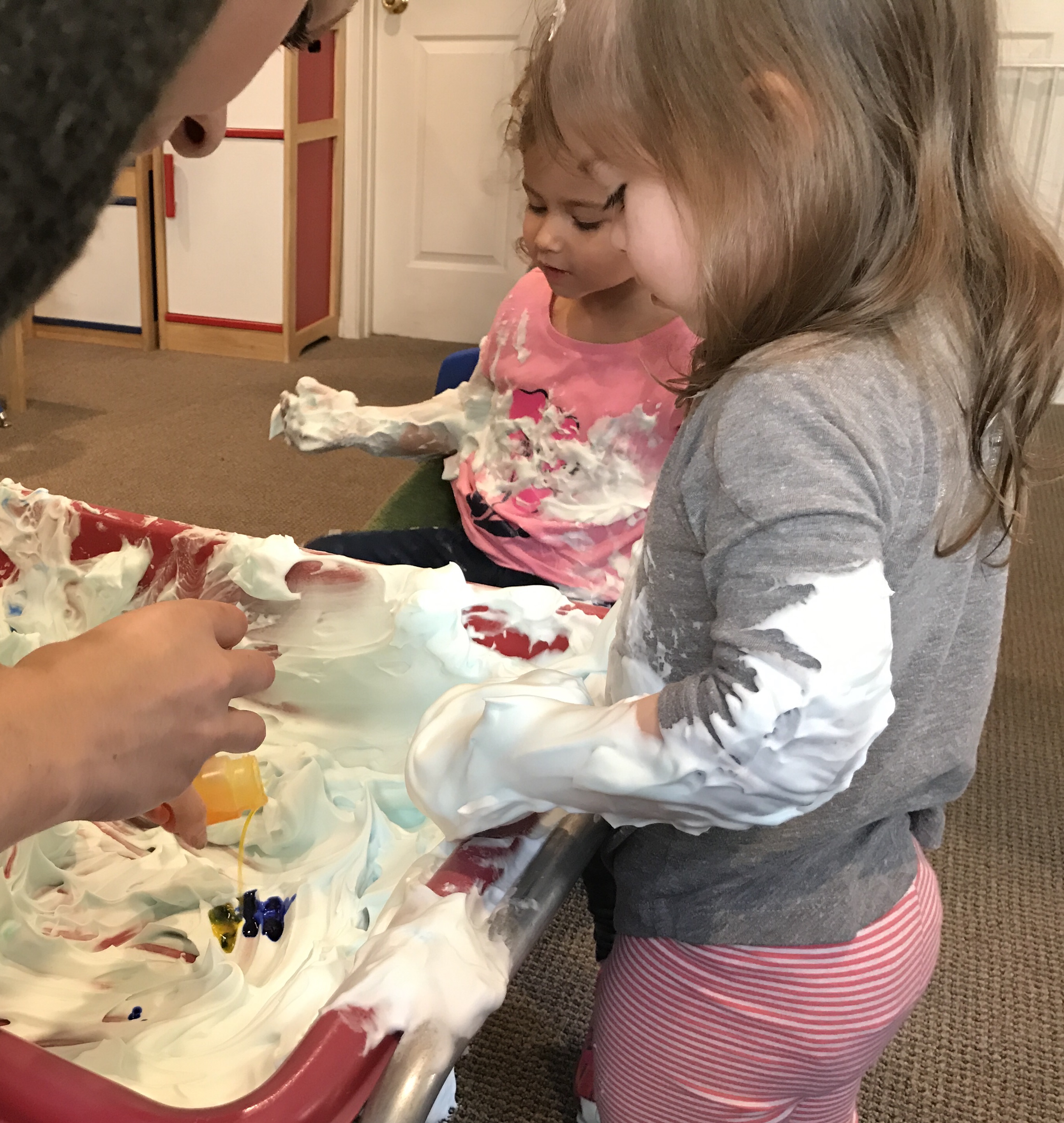 2 little girls mixinig yellow and green paints to make green shaving cream at early childhood development class