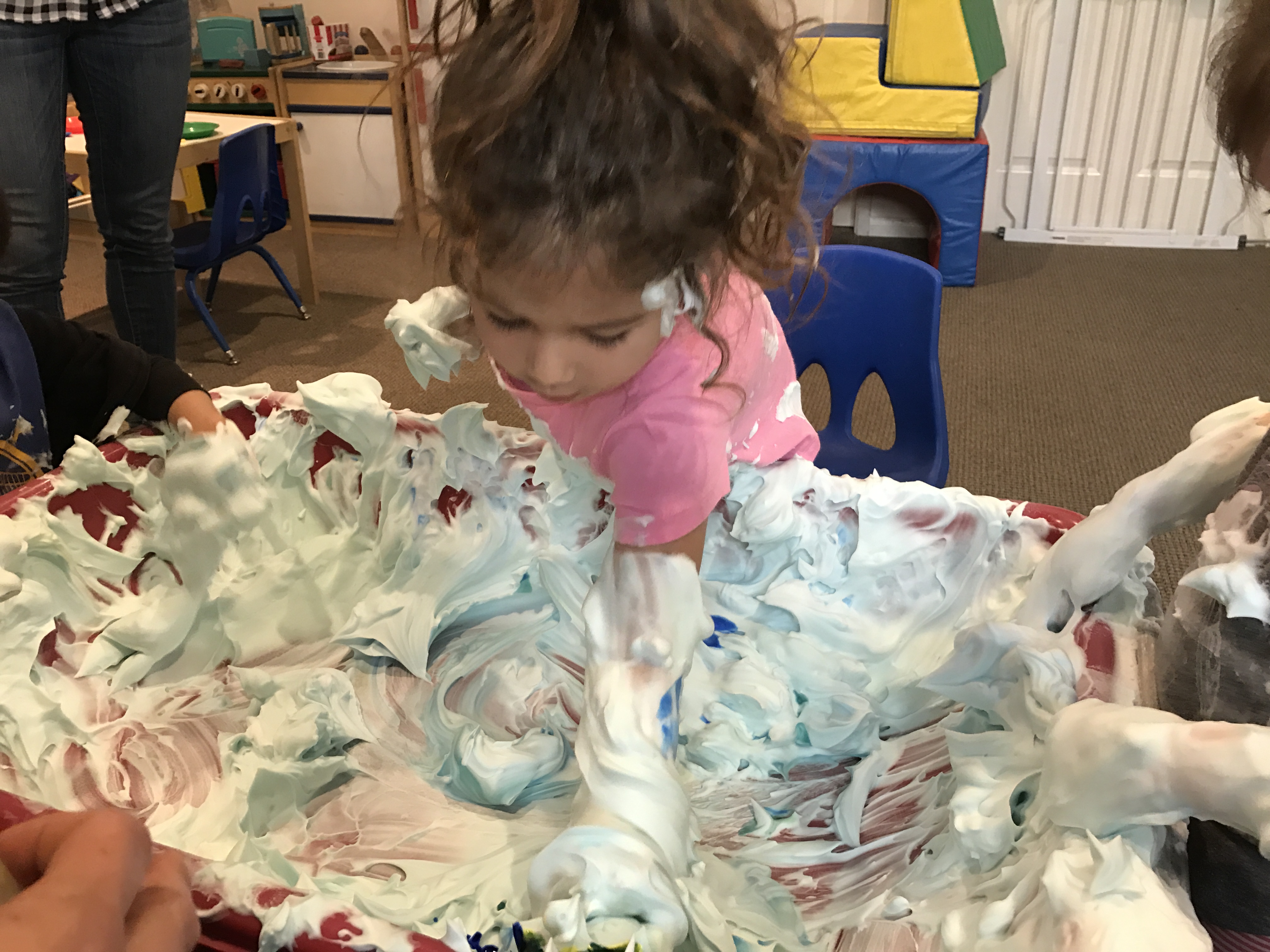girl mixinig yellow and green paints to make green shaving cream at early childhood development class
