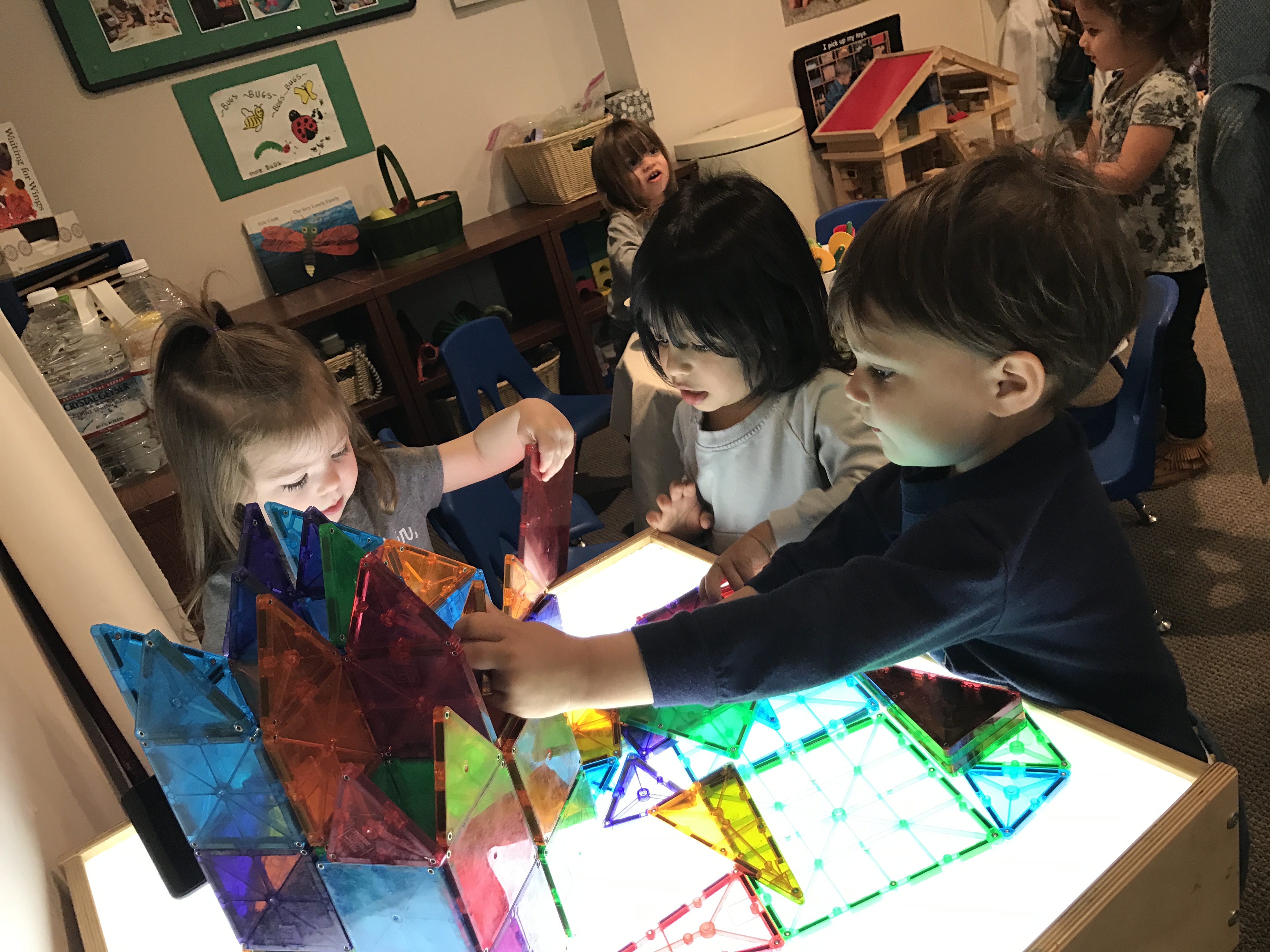 3 children playing together and sharing magnets table at early childhood development class