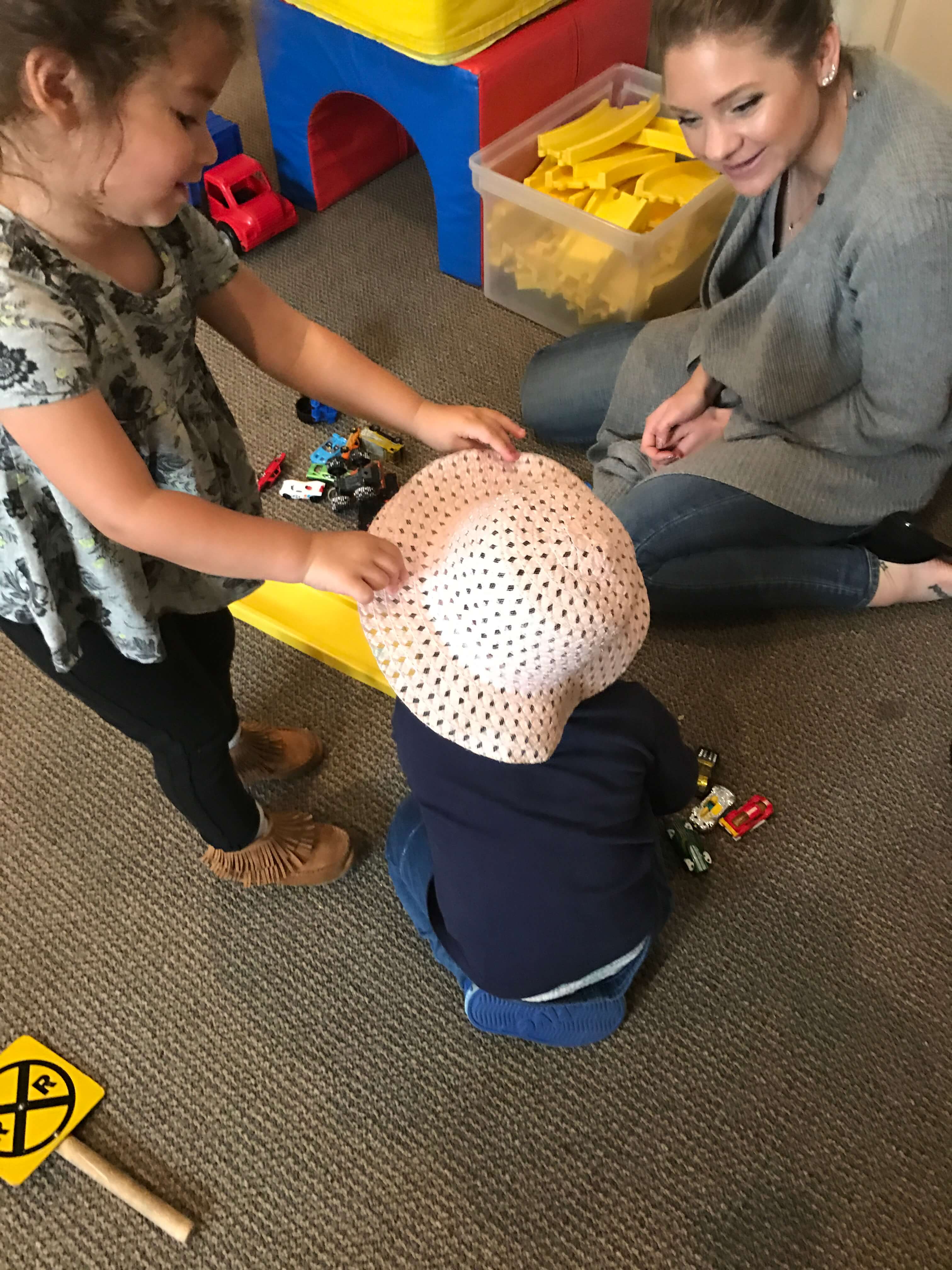 one girl putting a hat in a booy's head playing together with the teacher at early childhood development class