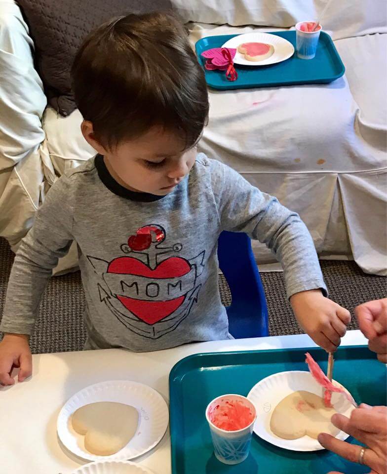 little boy frosting heart shaped cookies at early childhood development class