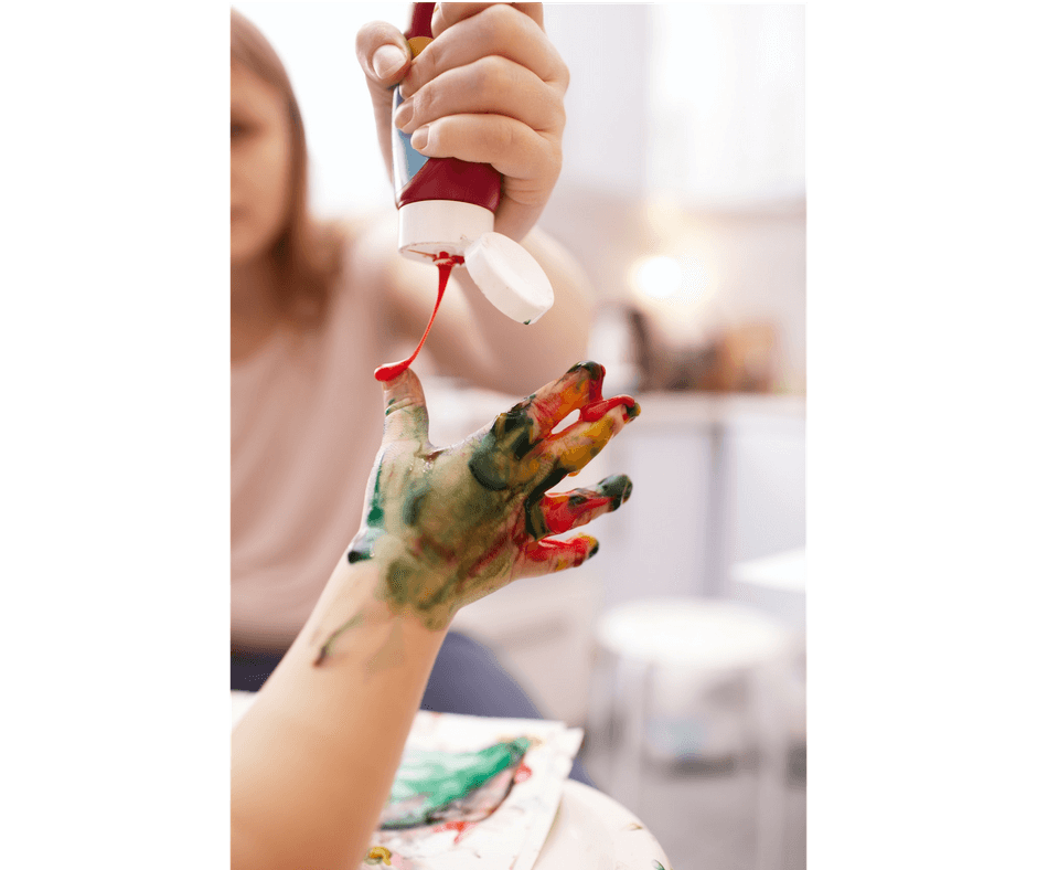 mother pouring paint in child's fingers for messy play