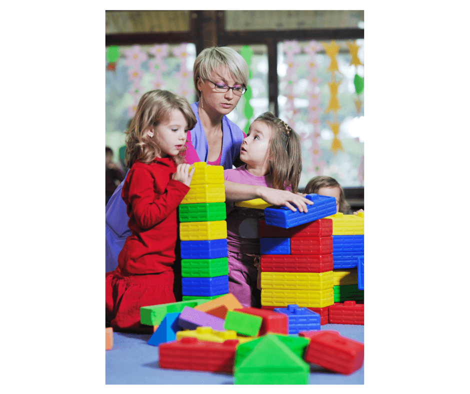 teacher helping 2 kids play together with blocks at preschool class