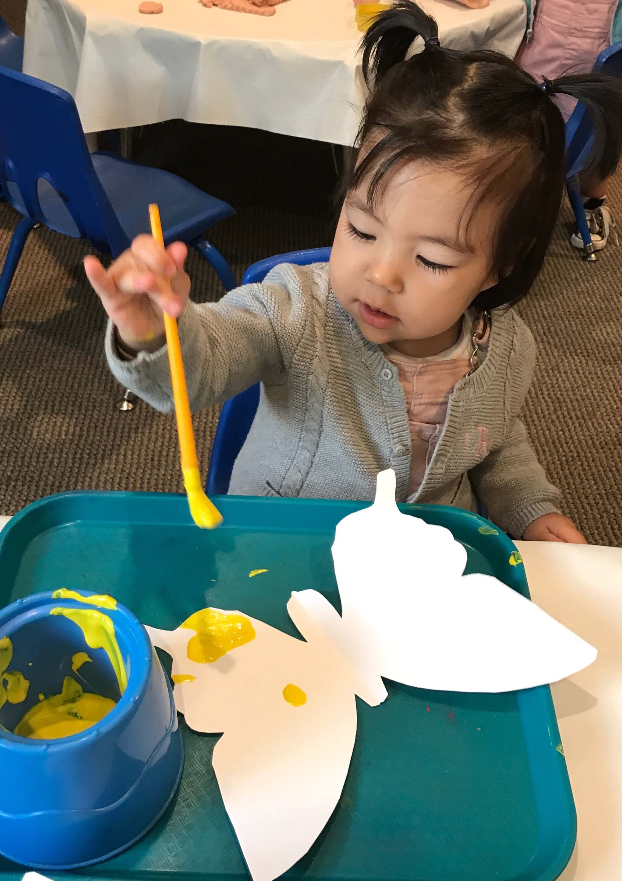 toddler painting butterfly shaped paper at early childhood development associates class