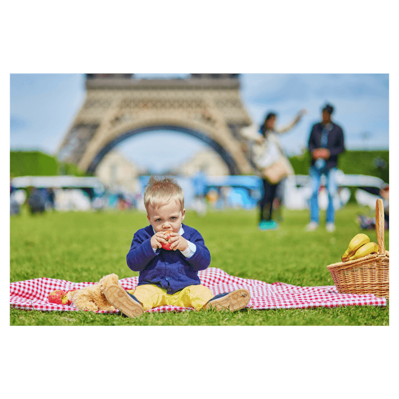 toddler sitting in blanket eating an apple in frot of eiffel tower in Paris