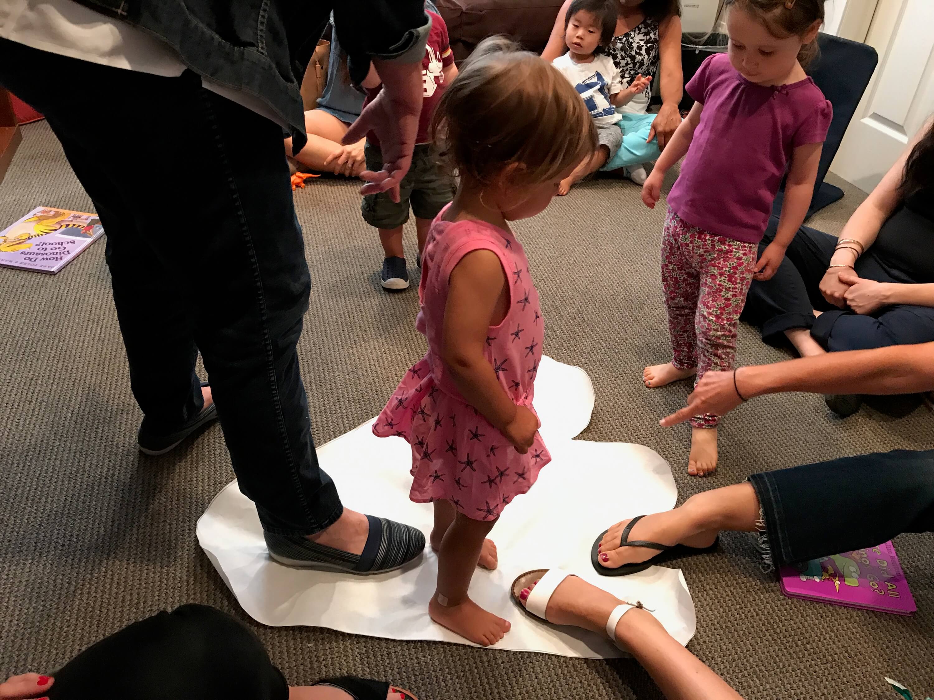 toddler measuring sizes of feet comparing to pig dinasour print on the floor at Early Childhood Development Associates's preschool prep class