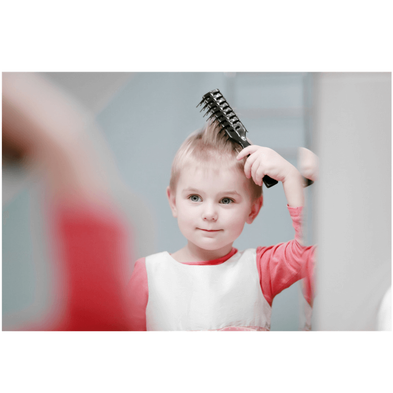 little girl in front of the mirror brushing her hair before going to school in the morning