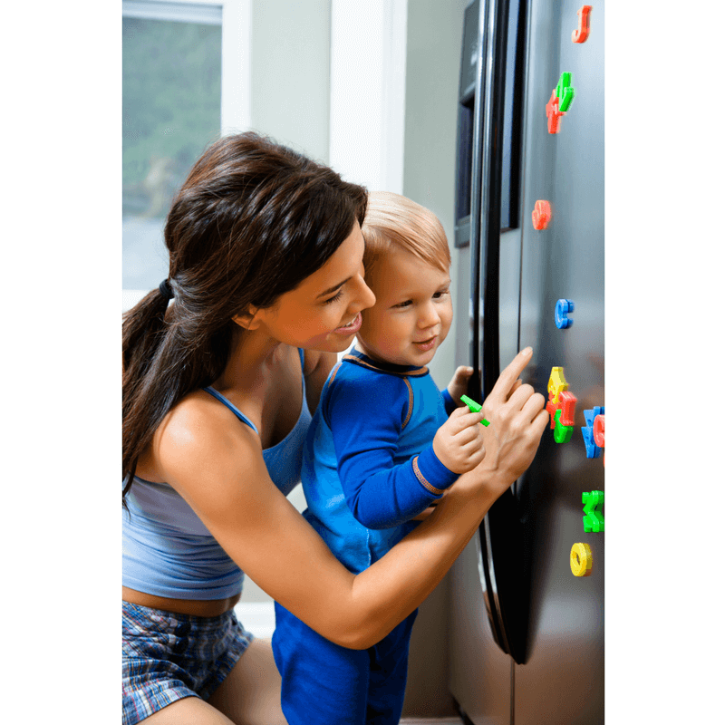 mother helping toddler son with magnets on the fridge